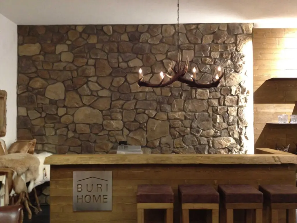 Rustikale Inneneinrichtung mit Steinwand, Holztresen und Geweihluster in gemütlichem Raum.