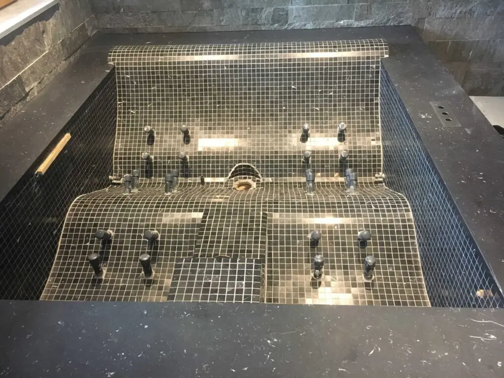 Luxuriöse Whirlpool-Wanne mit schwarzen Mosaik-Fliesen und zahlreichen Wasserdüsen für ultimative Entspannung im Spa.