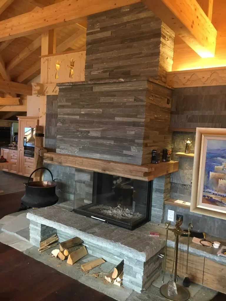 Moderner Kamin aus Naturstein und Holz in einem Wohnzimmer, dekoriert mit Holz und einem Kupferkessel.