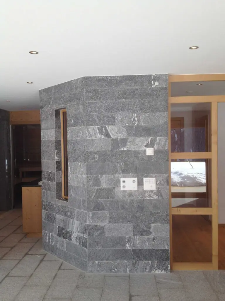 Moderner Innenraum mit grauer Steinwand und Holztür, stilvoll beleuchtet durch Einbaustrahler.
