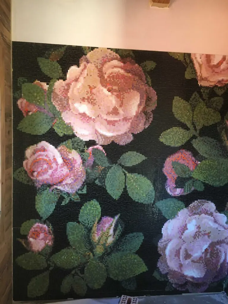 Mosaik-Wandbild mit großen, rosa Rosenblüten und grünen Blättern auf dunklem Hintergrund, dekorativ und kunstvoll.