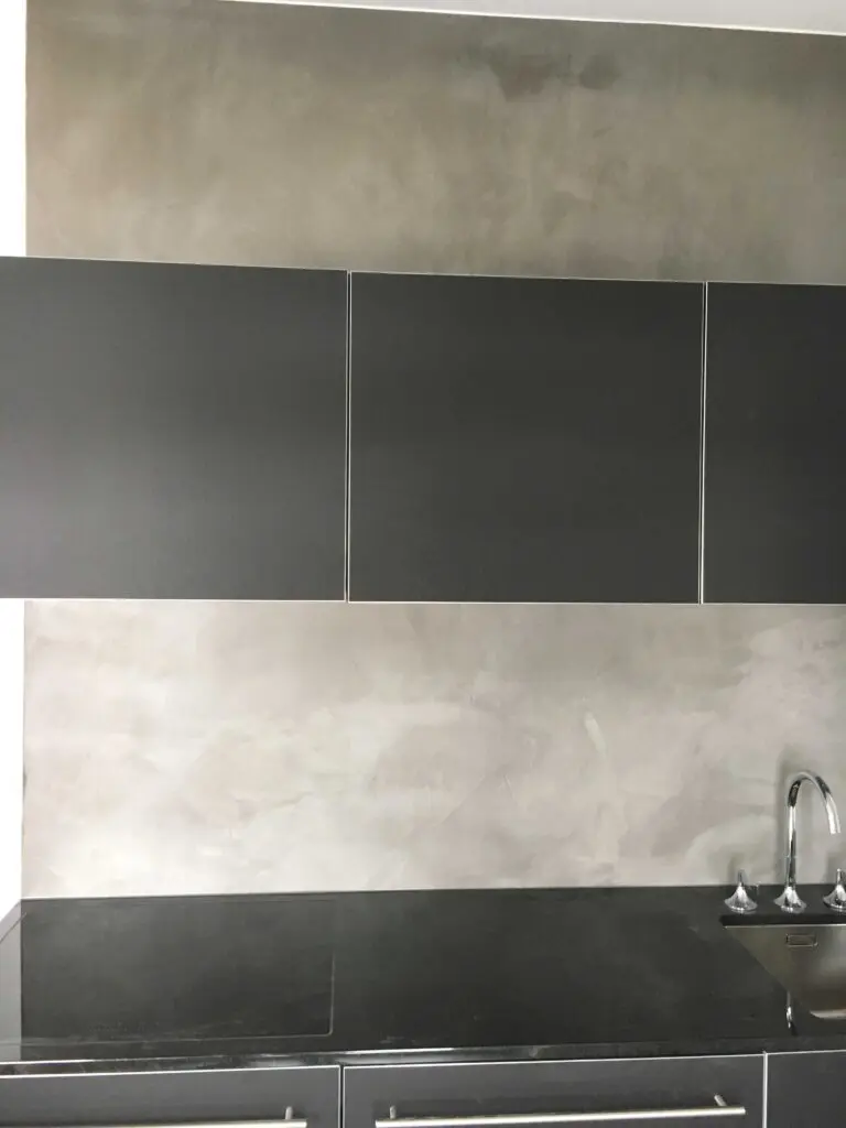 Moderne Küche mit dunklen Schränken, Edelstahlarmatur und grauer Betonwand. Minimalistisches Design.