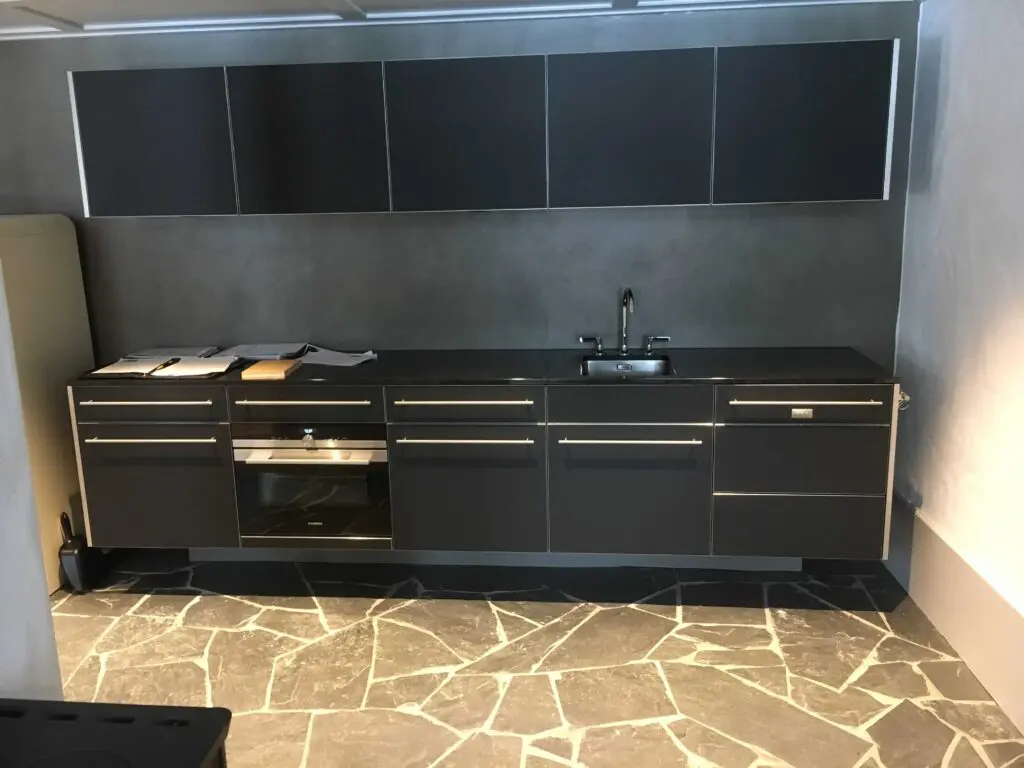 Moderne Küche mit dunklen Schränken, integriertem Ofen, Spüle und elegantem Steinboden.