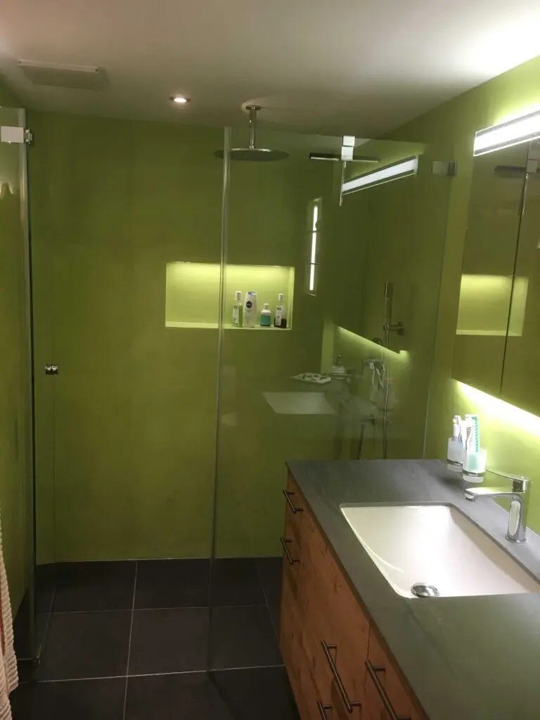 Modernes Bad mit grünen Wänden, Regenwalddusche und Holz-Waschtisch, minimalistisch und elegant gestaltet.