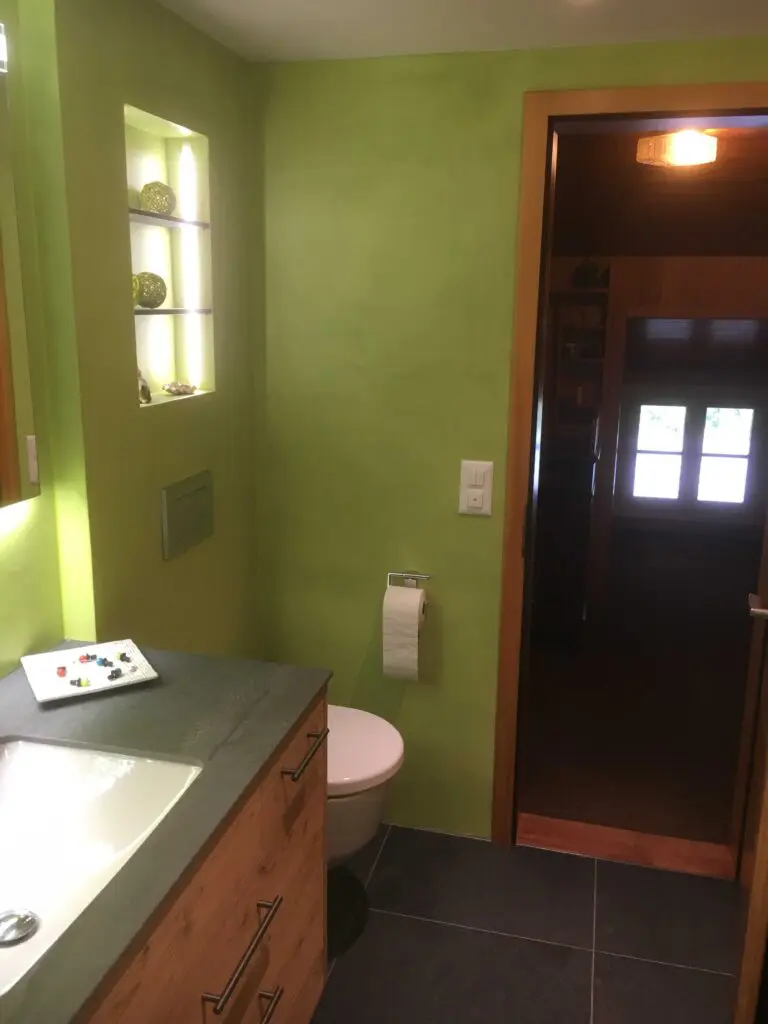 Modernes Badezimmer mit grünen Wänden, Waschtisch, WC und Dekorationen im Regal.