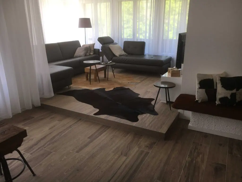 Moderner Wohnraum mit Ledersofas, Holzboden, Kuhfell-Teppich und stilvollen Beistelltischen.