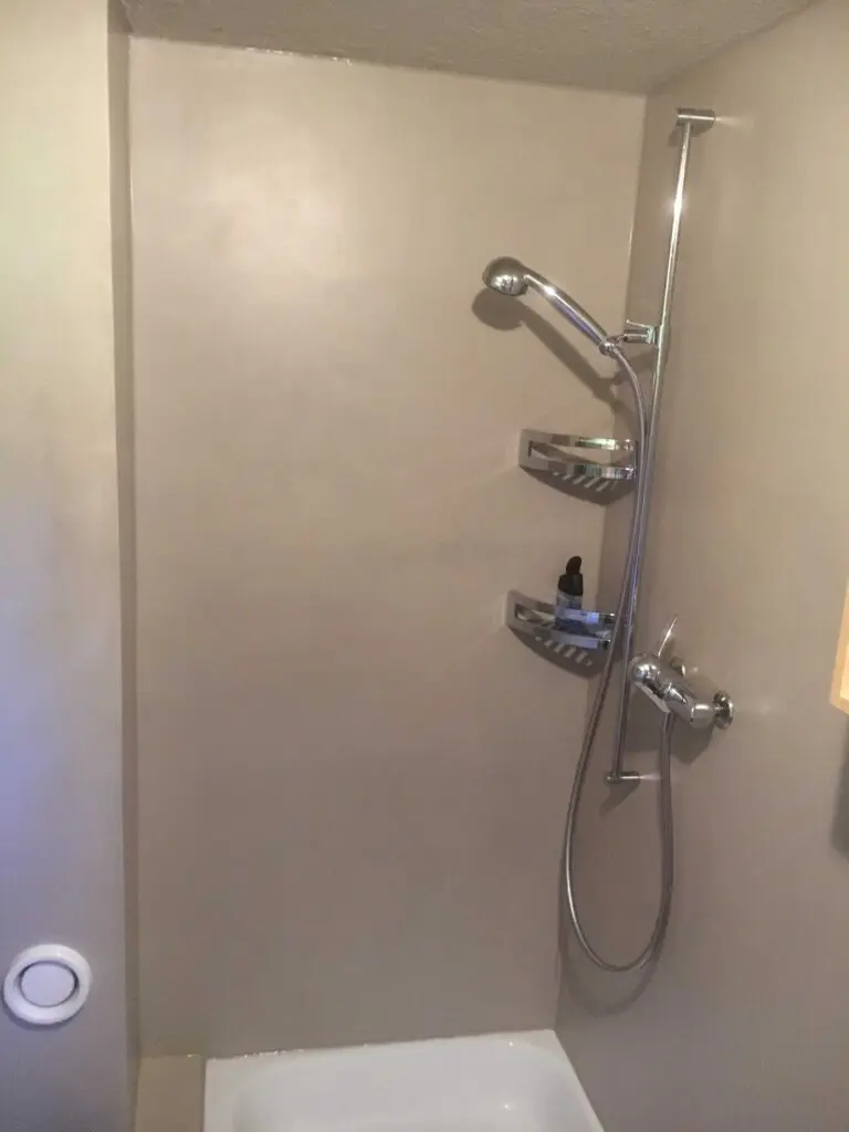 Dusche mit moderner Duschbrause und Regal in minimalistischer Badezimmerumgebung.