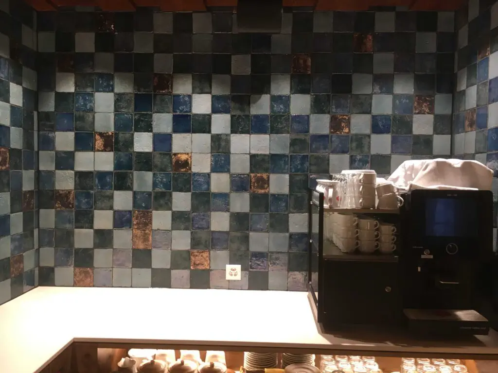 Kaffeemaschine vor blauer Kachelwand mit Regalen voller Tassen, stilvolle Caféecke in einem modernen Raum.