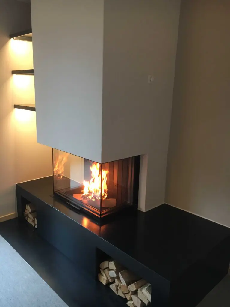 Moderner Kamin mit Glasfront in gemütlichem Wohnzimmer, Holzstapel darunter sichtbar.