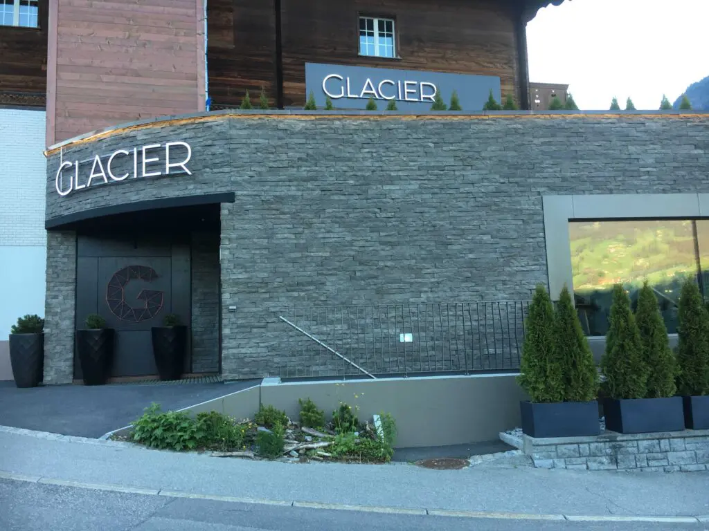 Eingang des Glacier Hotels mit moderner Steinwand und stilvoller Beschilderung, umgeben von grünen Pflanzen.
