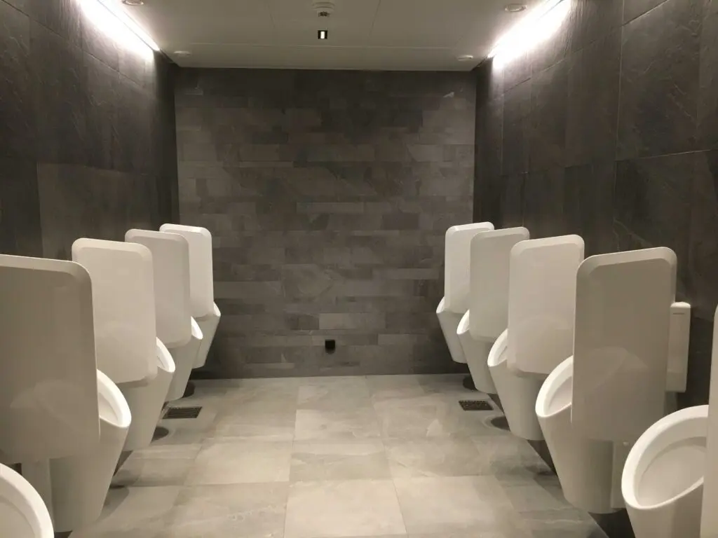 Moderne öffentliche Herrentoilette mit grauen Fliesen und weißen Urinalen in zwei Reihen.