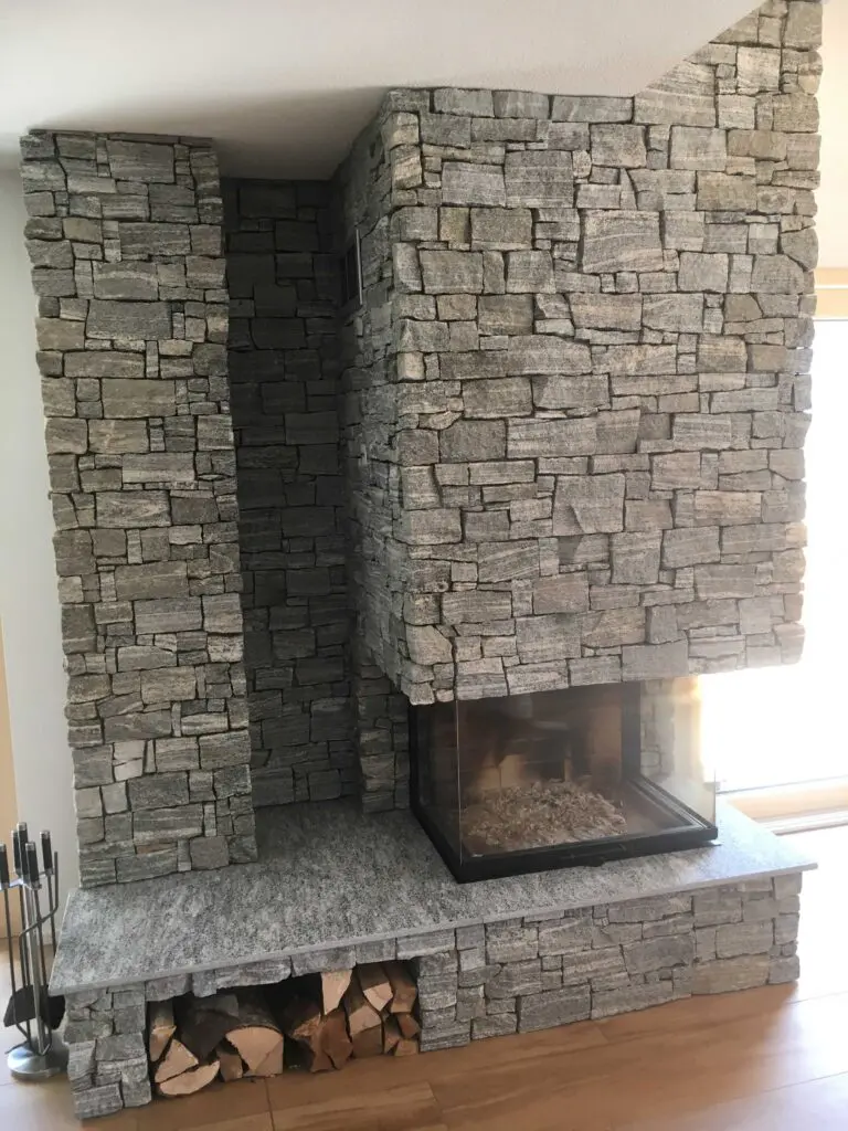Moderner Kamin aus Naturstein mit Holzlagerung darunter, ideal für gemütliche Abende im Wohnzimmer.