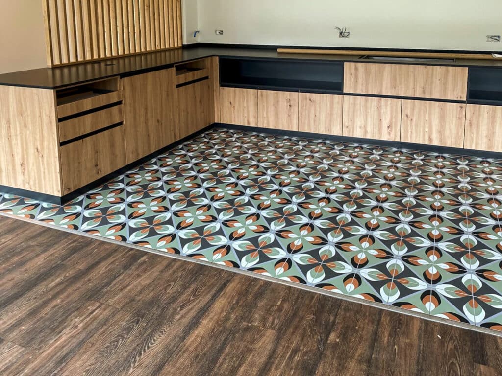 Moderne Küche mit gemustertem Fliesenboden und holzverkleideten Schränken, kontrastiert mit dunklem Laminat.